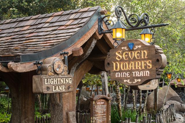 The entrance sign for Seven Dwarfs Mine Train at Magic Kingdom Park features rustic wood details, glowing lanterns, and a Lightning Lane queue marker.