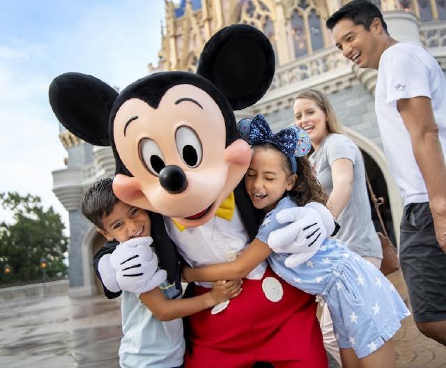 Two children joyfully hug Mickey Mouse in front of Cinderella Castle at Magic Kingdom Park, while their parents smile nearby, capturing a magical Disney moment.