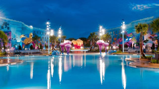 Nighttime view of The Big Blue Pool at Disney’s Art of Animation Resort, featuring vibrant Finding Nemo-themed sculptures, glowing jellyfish decorations, and colorful building murals under bright lights.